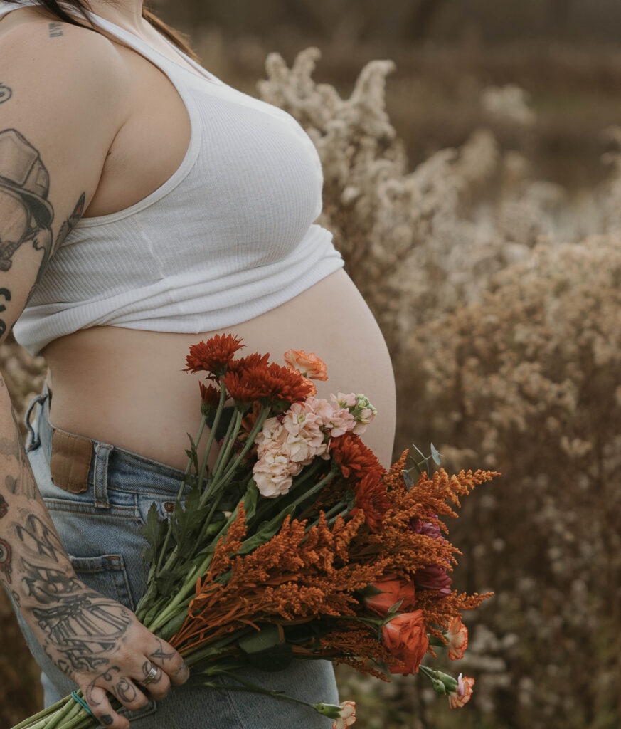 A close up of a mothers growing belly with a bouquet of wildflowers. 