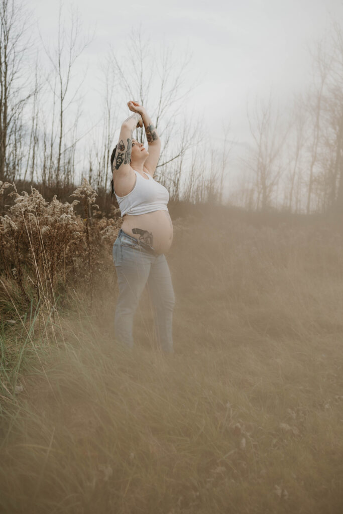 A peaceful bohemian style photo of a pregnant woman in a field posing, and looking up into the sky. 