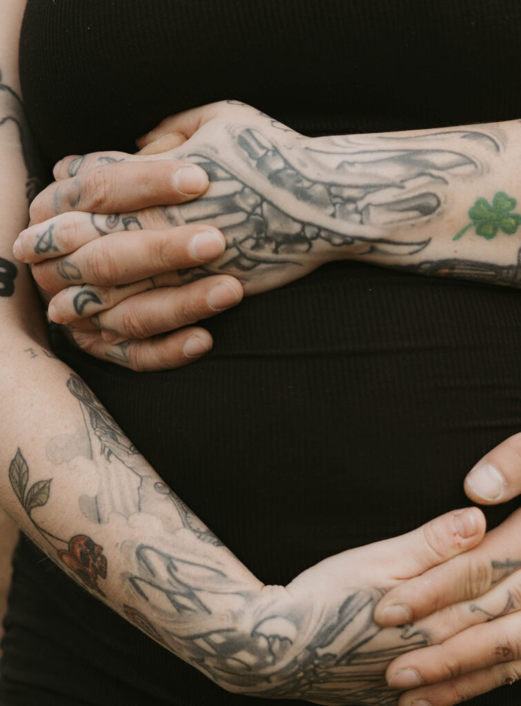 A close up shot of two parents intertwining and holding hands over her growing belly. 