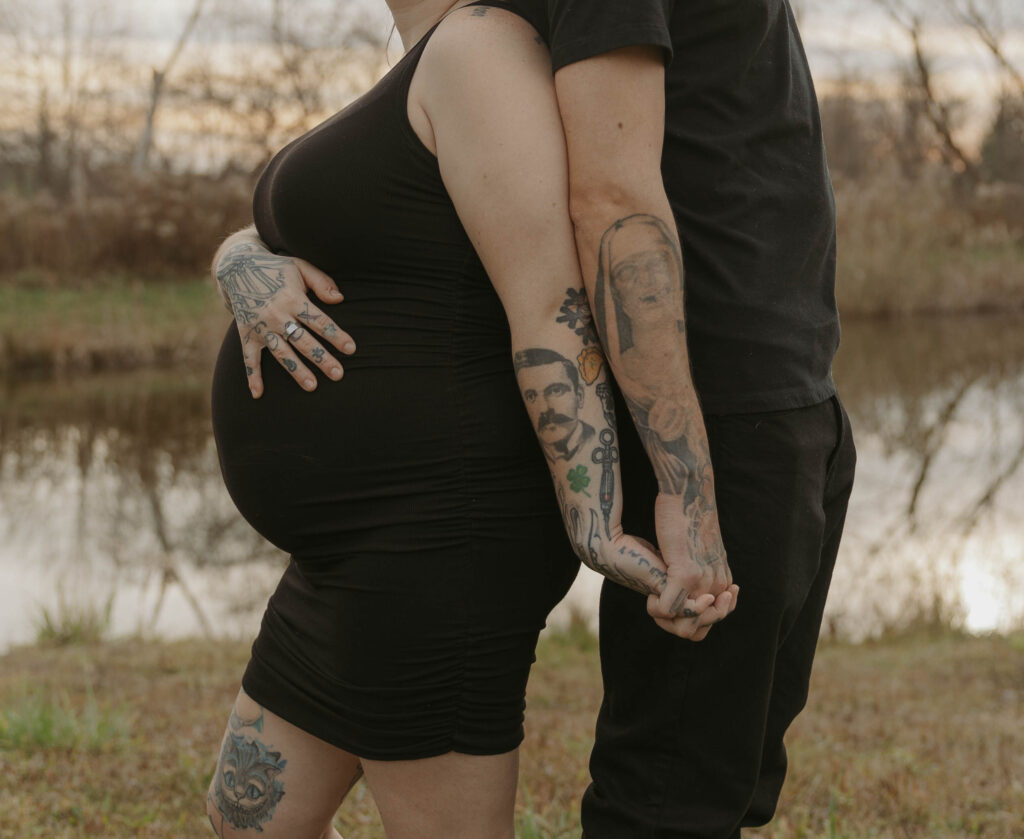 A close up image of two soon to be parents standing back to back and holding hands while imagining what their firstborn will be like. 